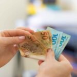 Mãos segurando notas de R$ 50 e R$ 100, representando precatórios e RPVs.