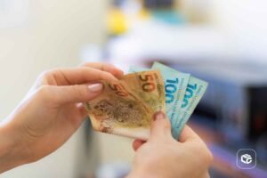 Mãos segurando notas de R$ 50 e R$ 100, representando precatórios e RPVs.