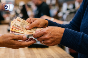 Mãos trocando notas de 50 reais, simulando pagamento de precatório.